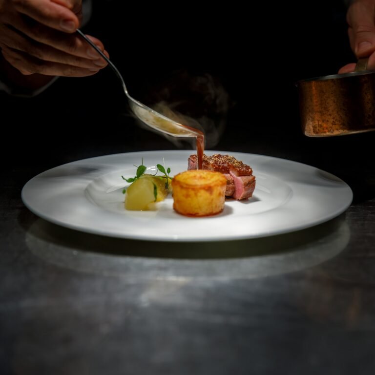 A chef pouring sauce over a plated dish