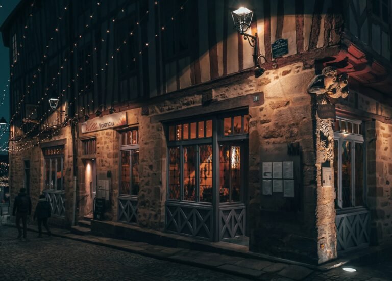 Lit shopfronts along an old harbour street at night