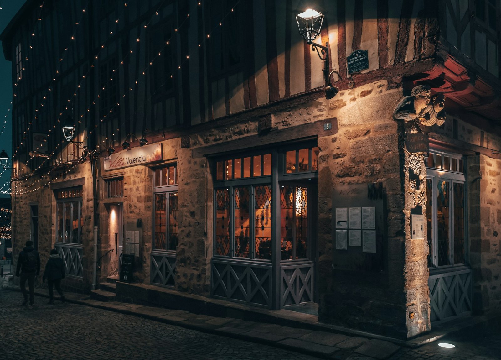 Lit shopfronts along an old harbour street at night